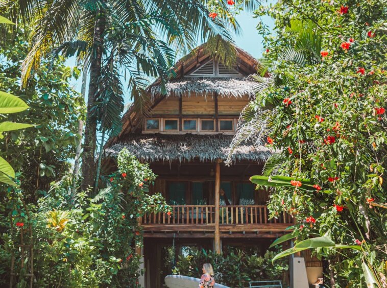 Photo by Jess Loiterton Woman in White Dress Standing Near Brown Wooden House